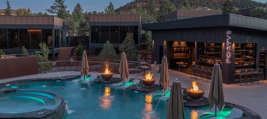 A pool with fire pits and umbrellas in front of a building with a mountain view