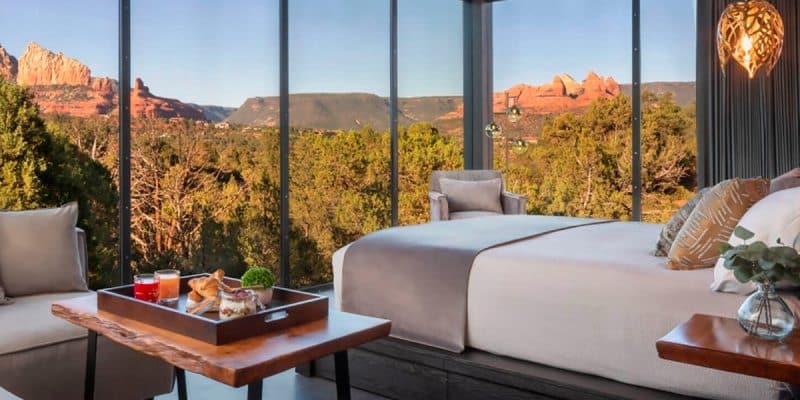 A luxurious bedroom with a large window showing a mountain view, a bed with white linens, and a breakfast tray on a wooden table.